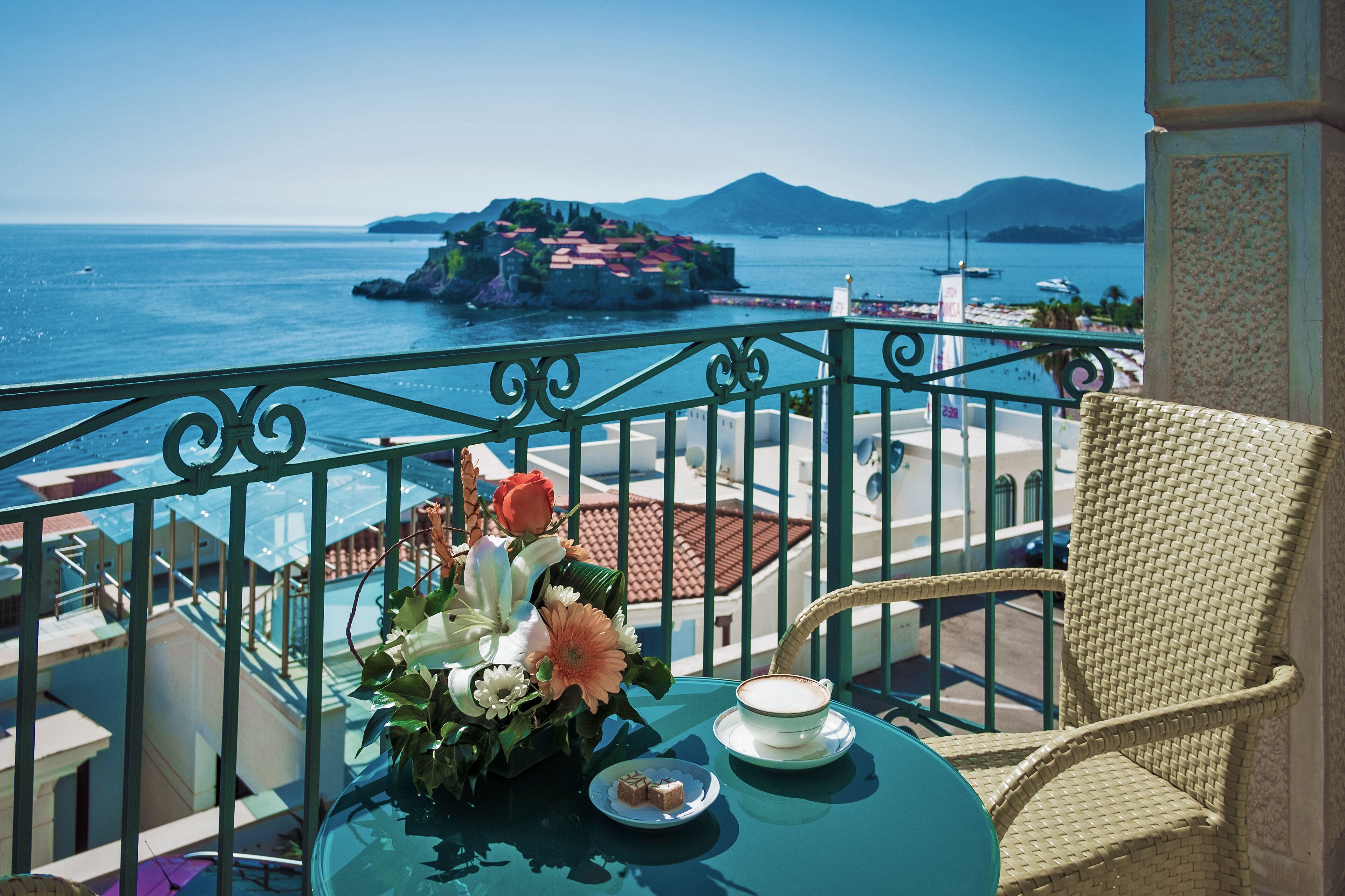 Un balcón con una mesa lista para el té, una silla de mimbre y vistas al mar y una isla distante.