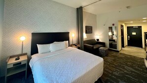 A hotel room with a large bed, two bedside lamps, a nightstand, a sofa, and a patterned carpet. - Home2 Suites by Hilton Rahway, NJ (Rahway)