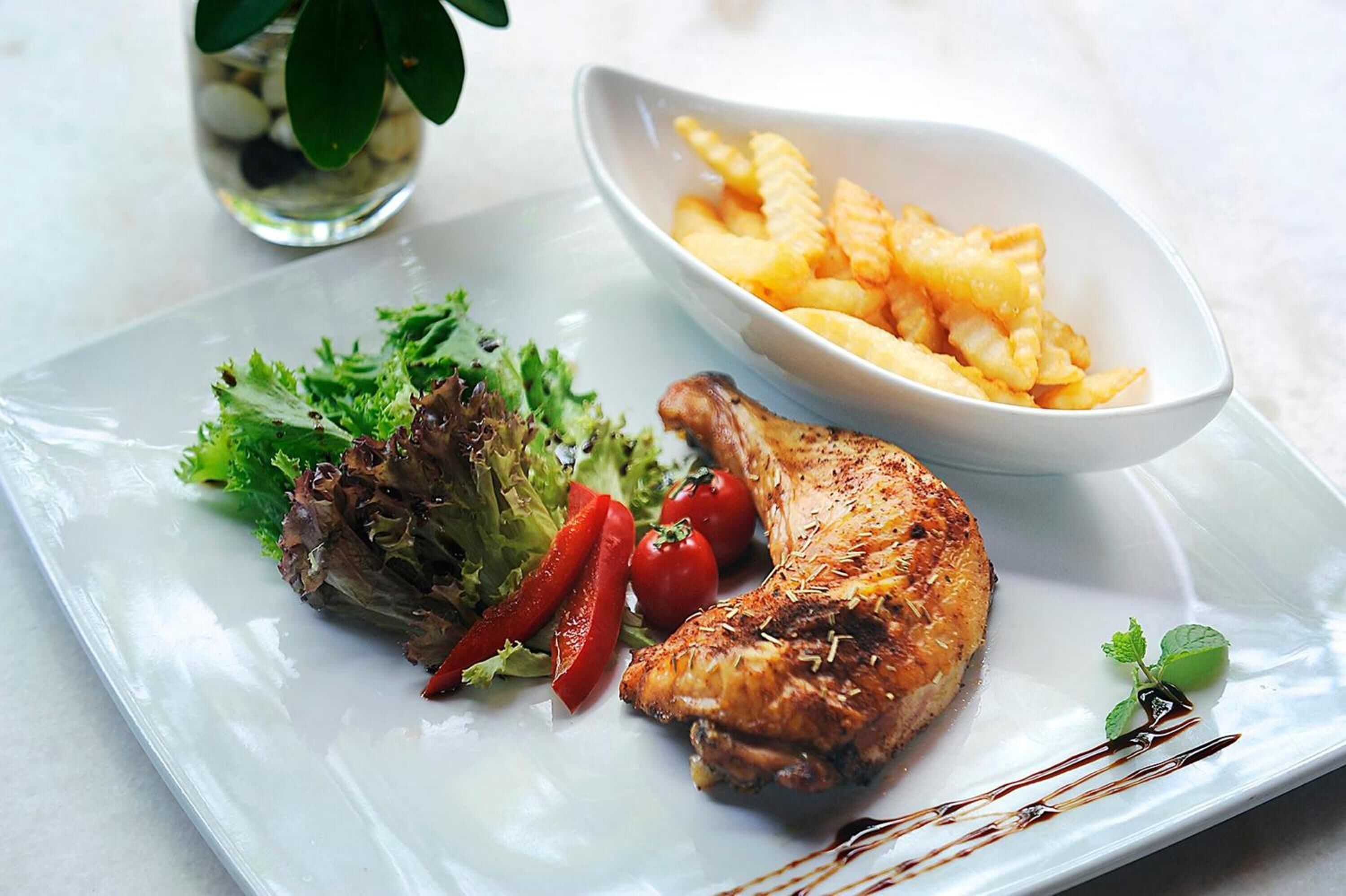 A plate with grilled chicken, vegetables, and French fries.