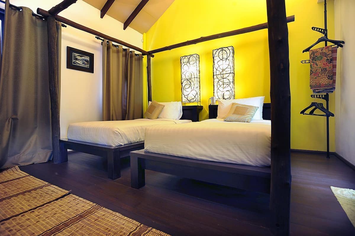 A room with two beds, wooden beams, a hanging light fixture, and a wall-mounted artwork.