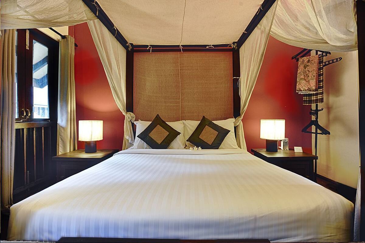 A large bed with a canopy, two bedside lamps, and a nightstand with a lamp.