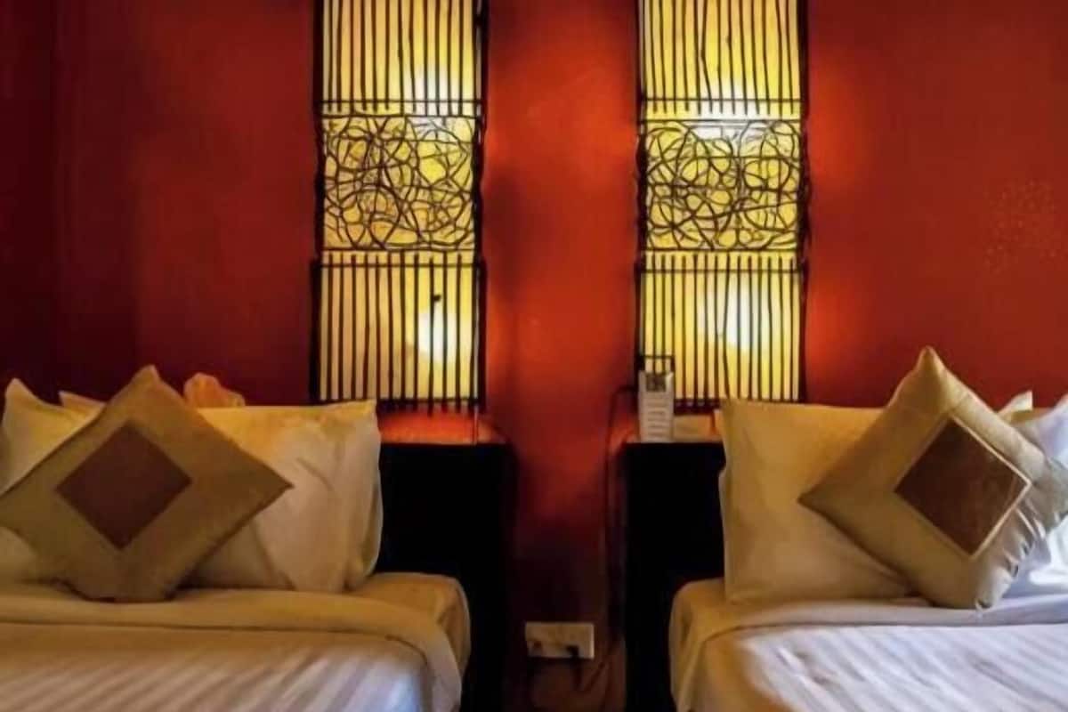 Two beds with headboards, a wall-mounted outlet, and a window with decorative bars.