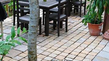 A terrace with wooden tables and chairs, surrounded by potted plants and a small tree.