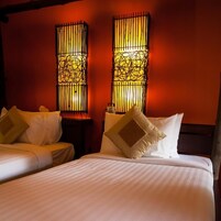 Habitación de hotel con dos camas, cada una con ropa blanca de cama y almohadas. Hay dos lámparas de pared con diseños elaborados.