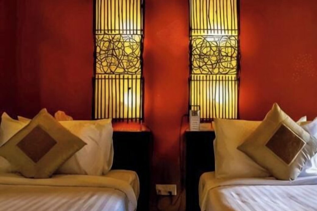 Two beds with headboards, a wall-mounted outlet, and a window with decorative bars.