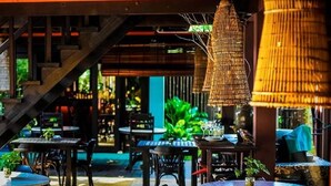 An indoor dining area with round tables and chairs, a staircase, and hanging lamps. - The Village House (Kuching)