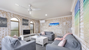 A modern living room with a white ceiling fan, grey sofas, a white coffee table, and a TV on a white stand. - Coast Inn Motel (Ballina)