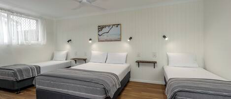 Une chambre avec trois lits, un ventilateur de plafond et un tableau au mur.