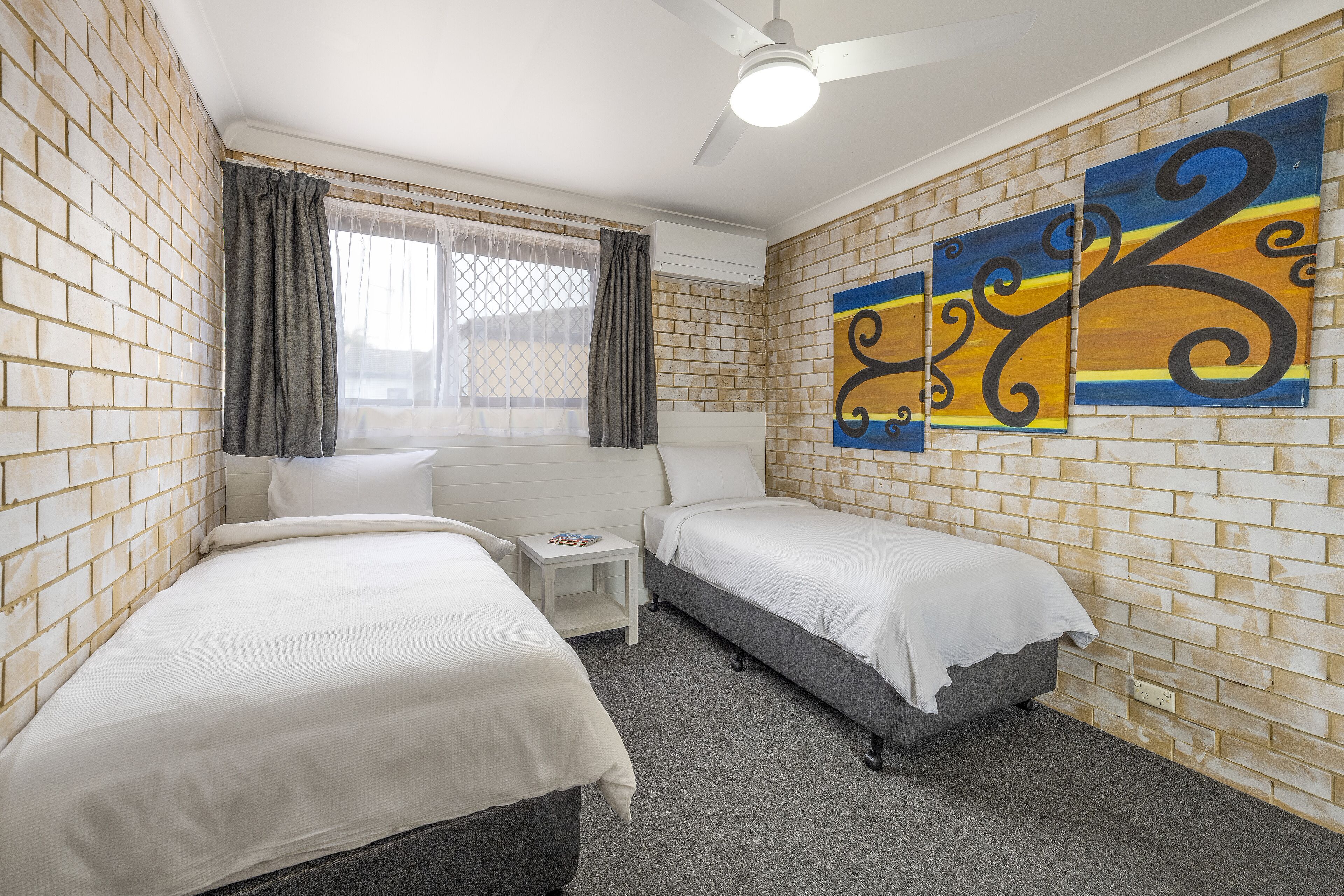 A room with two beds, a small table, and a ceiling fan.