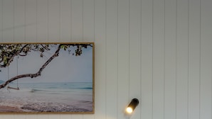A bed with white bedding, a wall-mounted picture of a beach scene, a bedside table, and a wall socket. - Coast Inn Motel (Ballina)