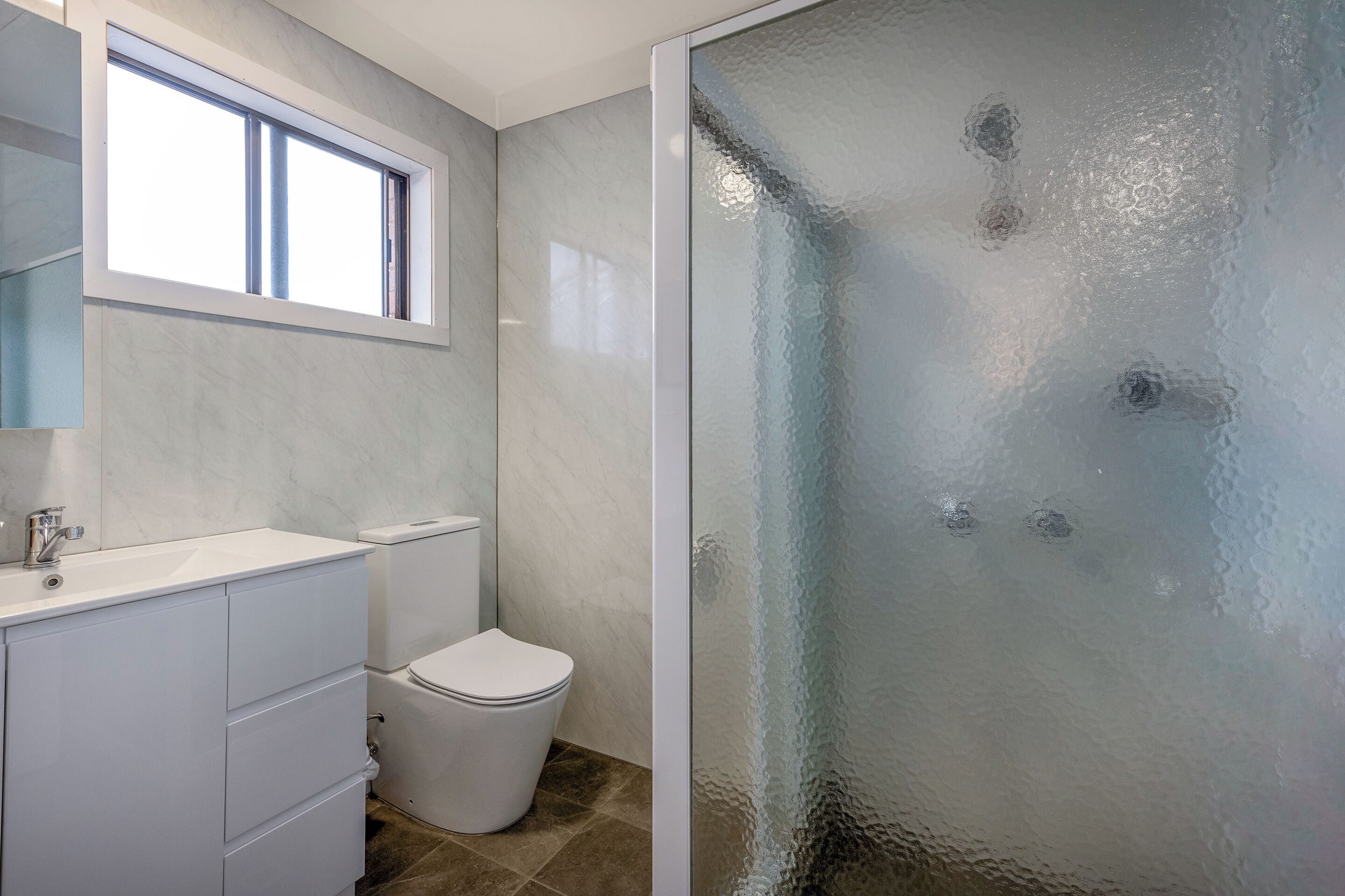 A bathroom with a white vanity, a toilet, and a glass shower enclosure.