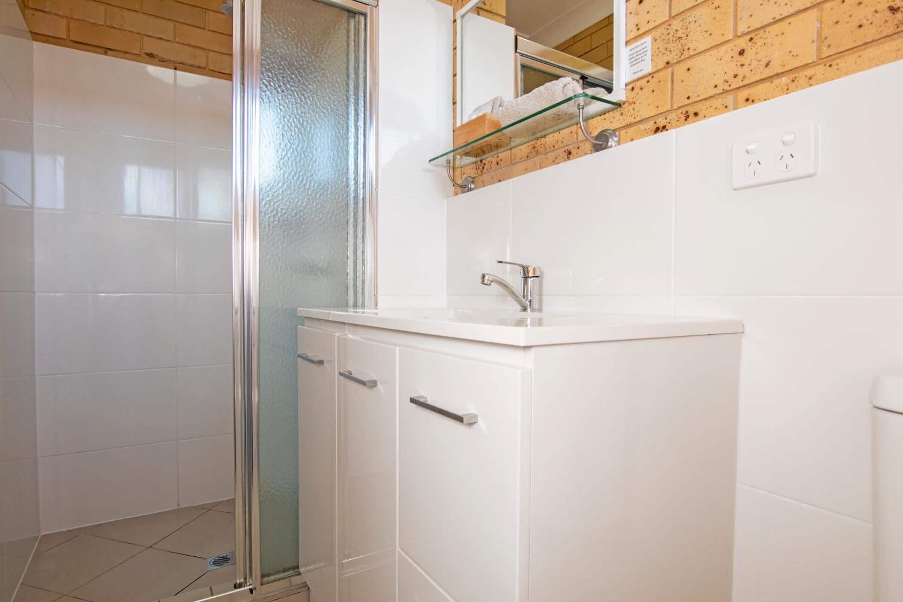 Une salle de bain avec une douche à parois de verre, un lavabo blanc avec un miroir au-dessus et un panneau mural en bois.