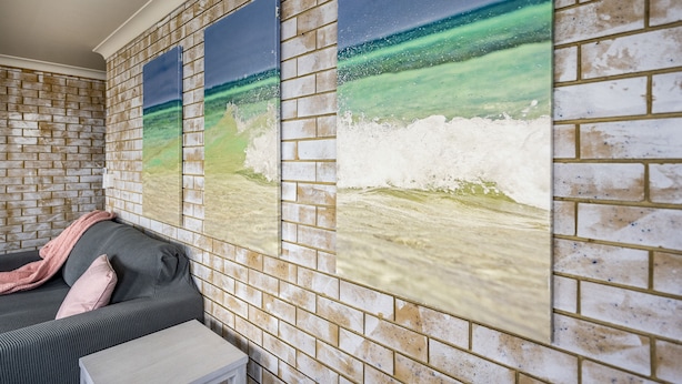 A room with a brick wall, a grey sofa, and a small white table. - Coast Inn Motel (Ballina)