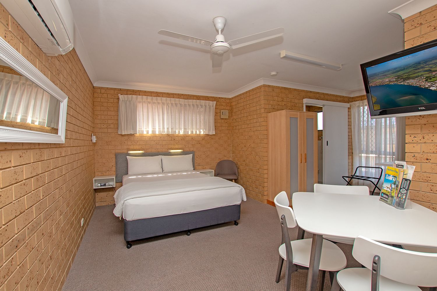 Habitación de hotel con cama, escritorio, sillas, televisor y ventana con cortinas.