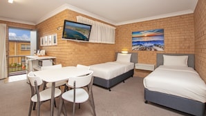 A hotel room with a brick wall, a TV, a desk with chairs, a bed, and a painting of a sunset. - Coast Inn Motel (Ballina)