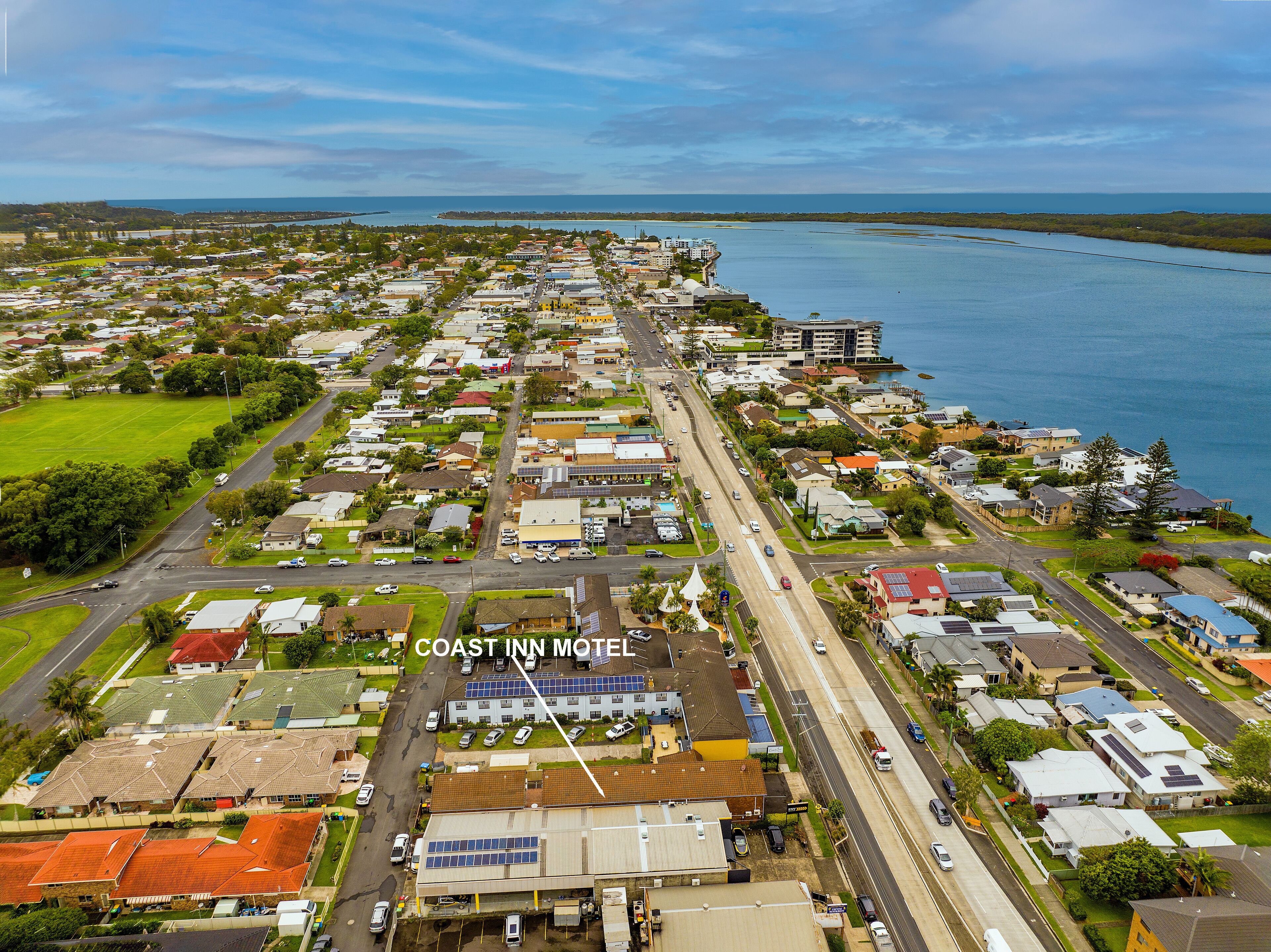 An aerial view of a coastal town with a prominent motel named "COAST INN MOTEL" featuring a central road, residential buildings, and a marina.