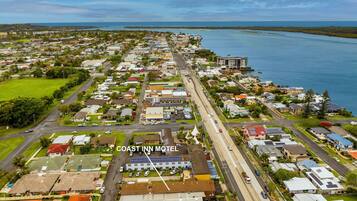 An aerial view of a coastal town with a prominent motel named "COAST INN MOTEL" featuring a central road, residential buildings, and a marina.