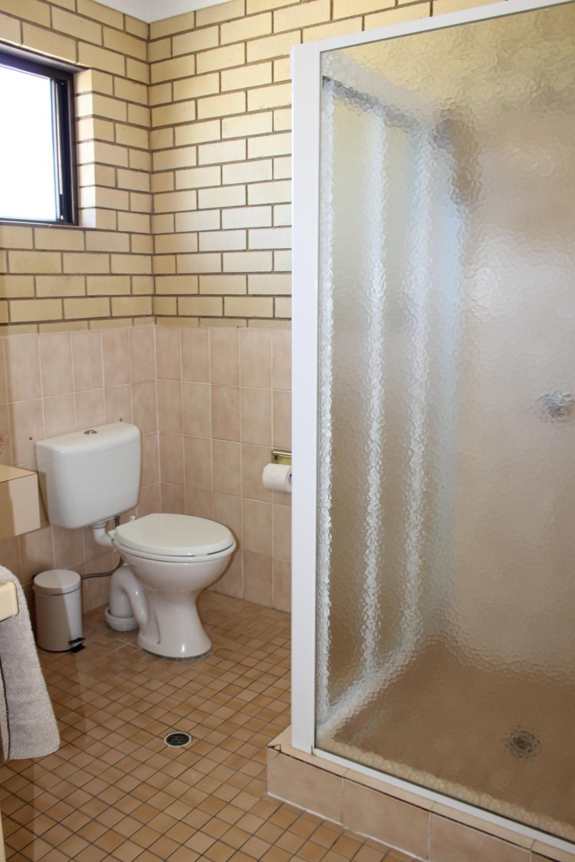 A bathroom with a toilet, a trash bin, a towel, and a glass shower enclosure.