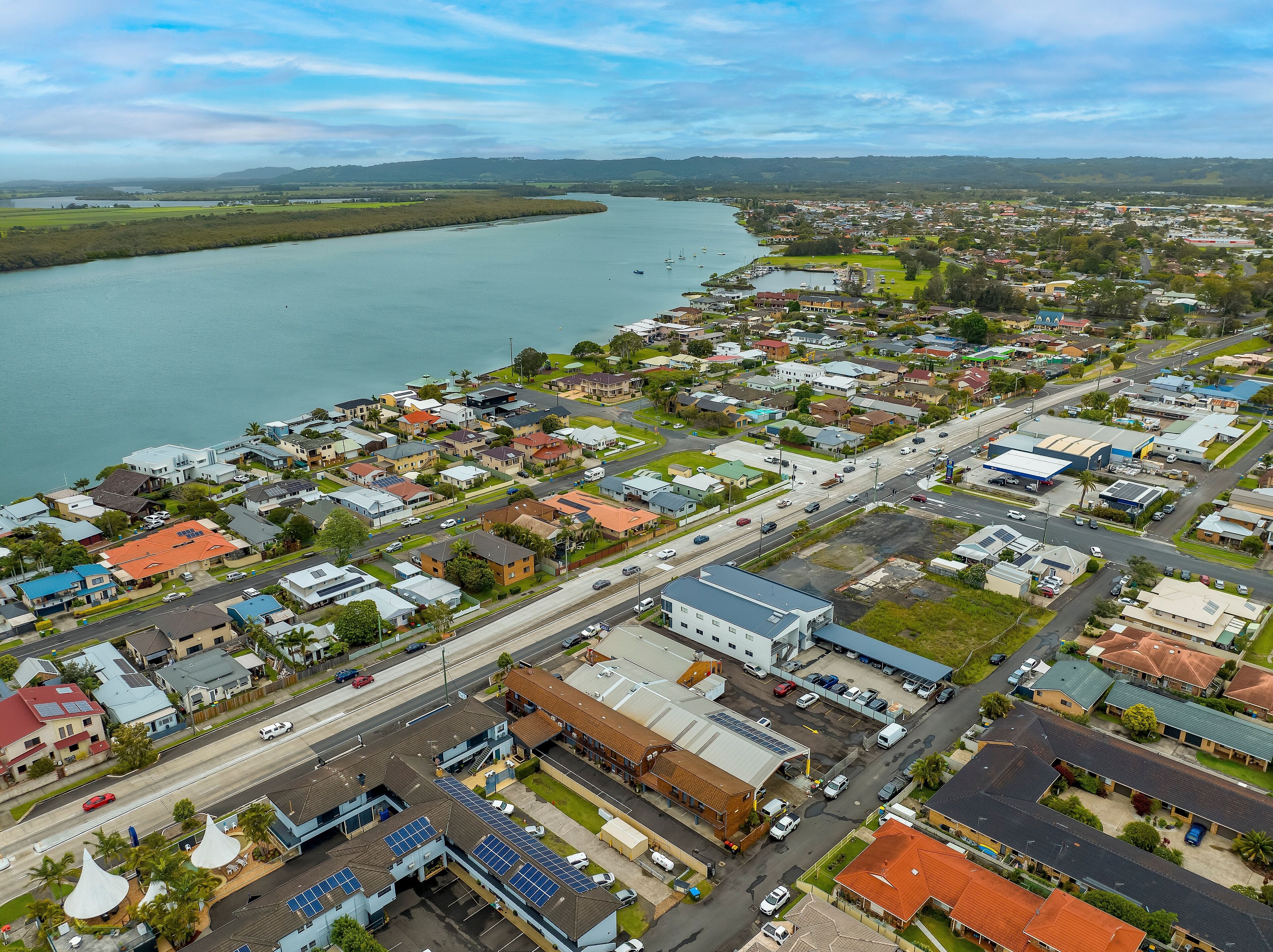 An aerial view of a coastal town with residential buildings, a marina, and a road running through the center.