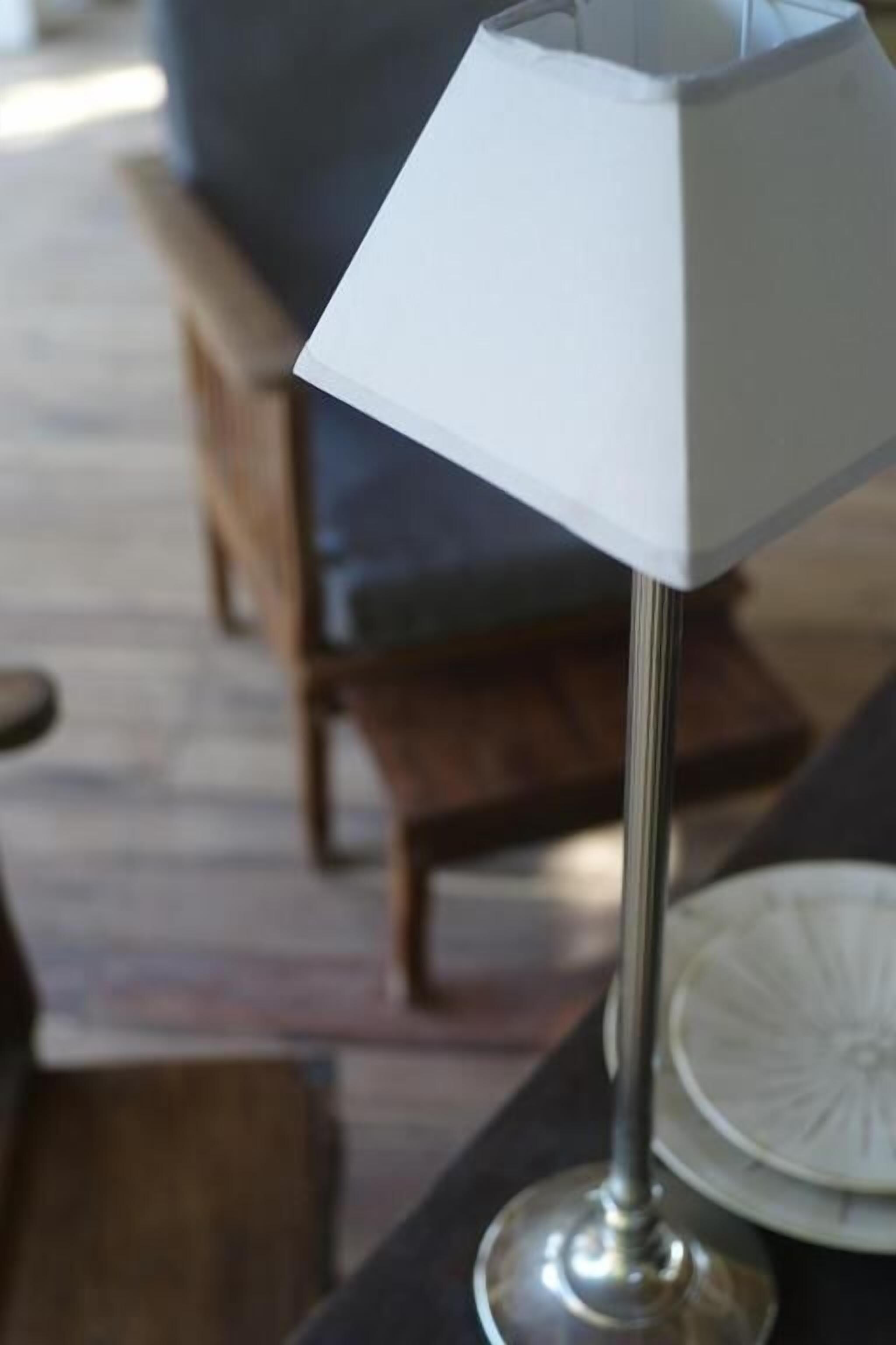 Een tafel met een witte tafelkleed, een metalen tafellamp en een wit bord met een decoratief ontwerp.