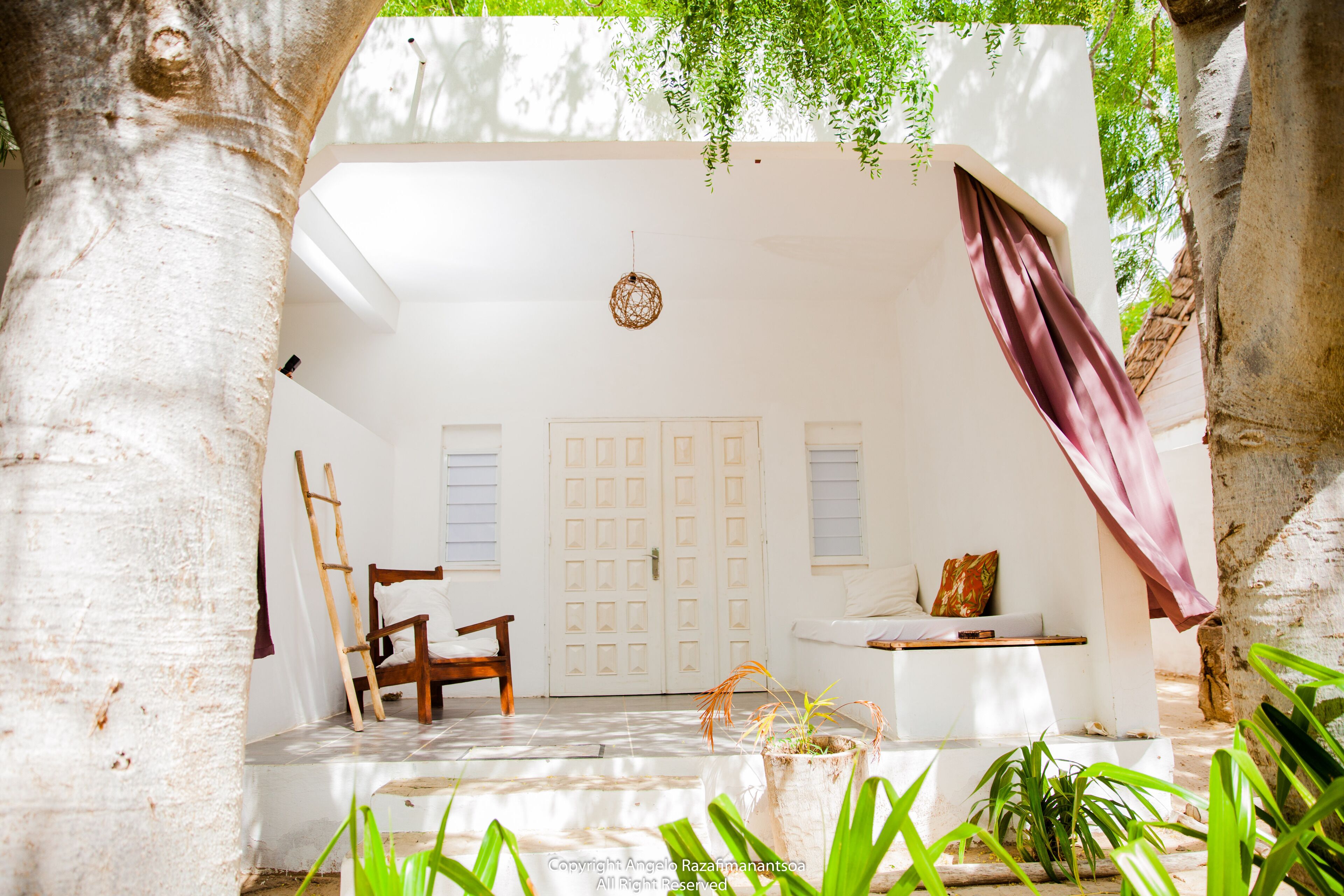 Una habitación con paredes blancas, una silla de madera, una mesita y una lámpara colgante.