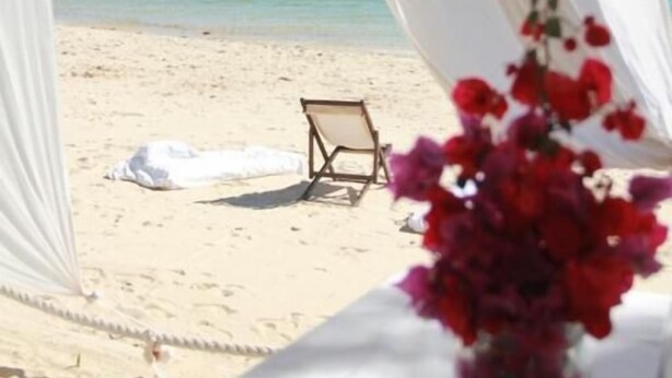 A beach setting with a white canopy, a table with a vase of red flowers, and a chair on the sand. - Princesse du Lagon (Ifaty)