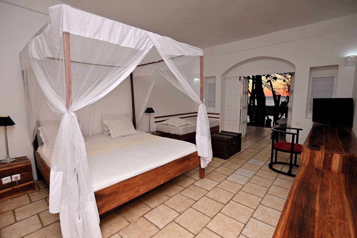 Een slaapkamer met een hemelbed, een houten nachtkastje, een bijzettafeltje, een stoel en een televisie.