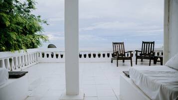 A terrace with white tiled flooring, two wooden chairs, and a bed with white bedding.