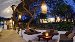 An outdoor seating area with sofas and tables, surrounded by trees and a building in the background. - Princesse du Lagon (Ifaty)