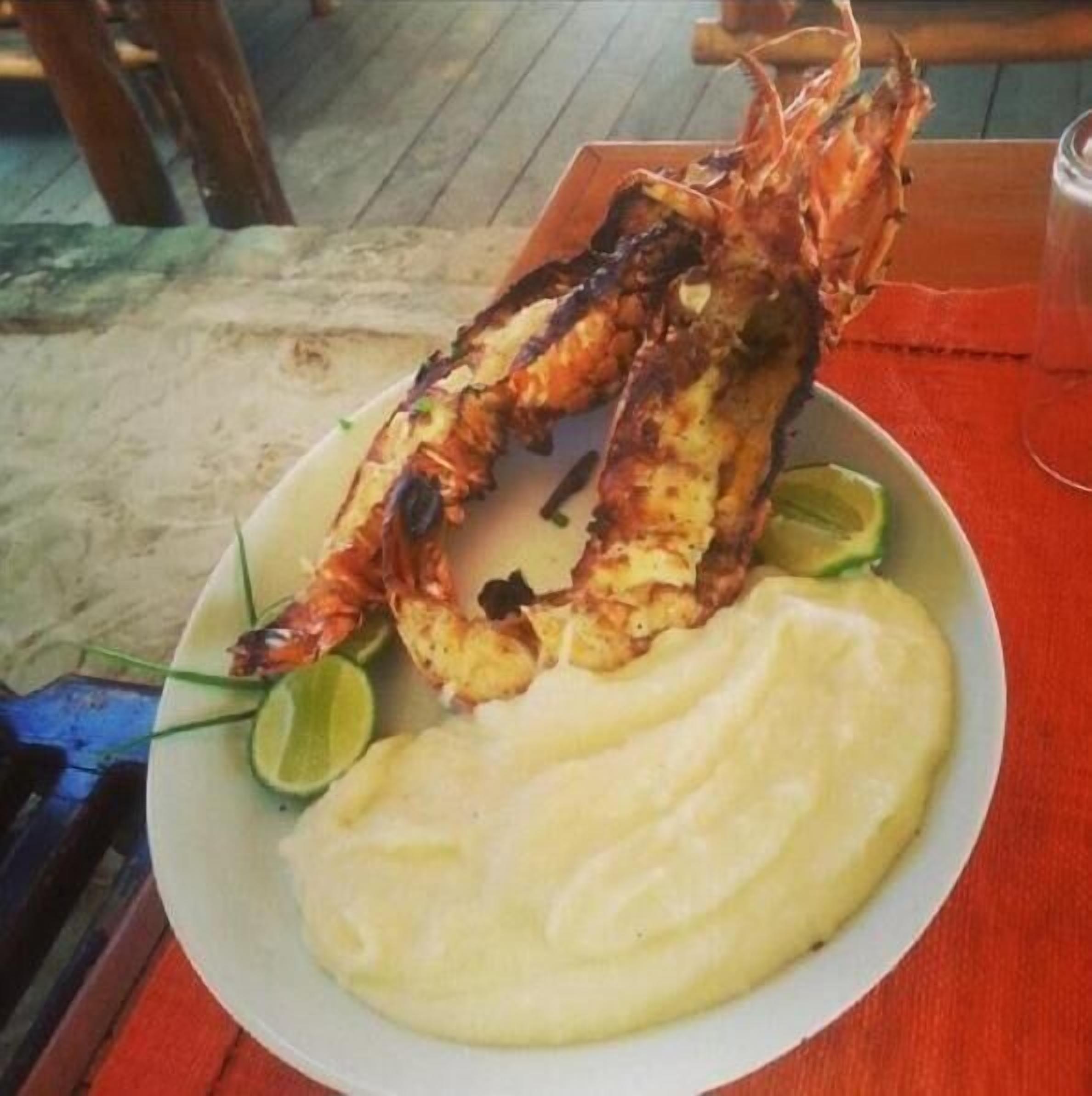 Un plato con cola de langosta a la parrilla, puré de papas y gajos de limón.