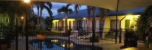 A pool area with a curved edge, surrounded by a fence and potted plants. - Peppercorn Motel (Clermont)