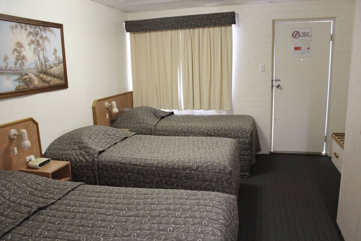 A hotel room with two beds, a painting on the wall, a window with curtains, a door with a sign, and a bedside table with a lamp.