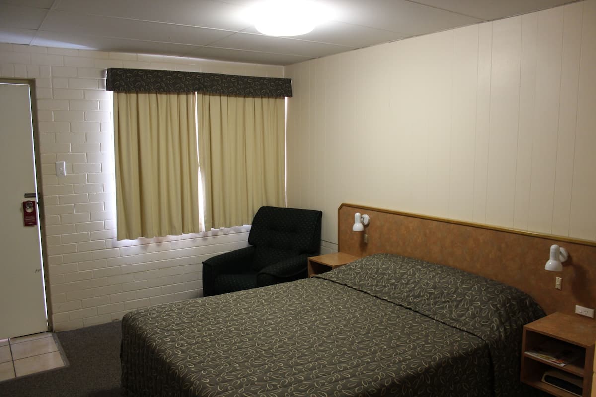 A hotel room with a bed, a chair, a nightstand, and a window with curtains.