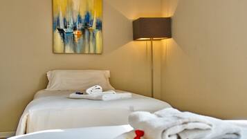 Una habitación de hotel con una cama, un cuadro de veleros, una lámpara y toallas.