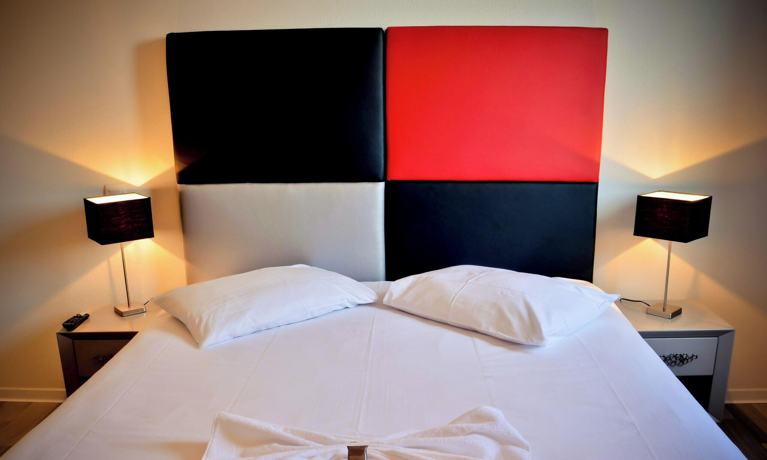 A hotel room with a large bed, two bedside tables, and two wall-mounted lamps.