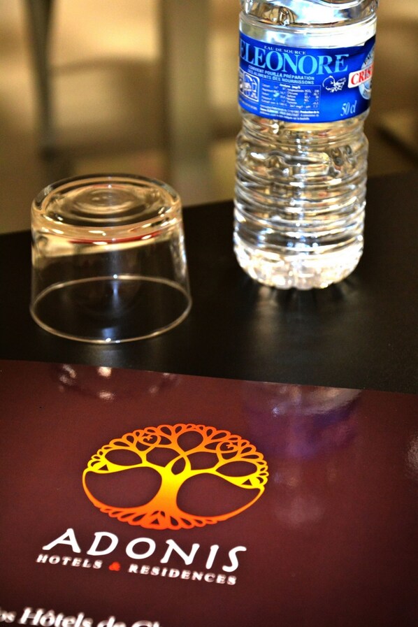 A bottle of Eleonore water and a glass on a table, with the Adonis Hotels logo below. - Adonis Hôtel Bayonne (Lahonce)