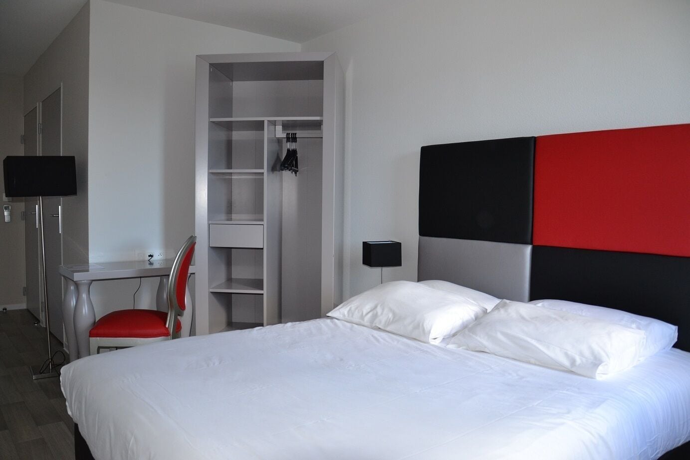 Hotelkamer met een bed, een bureau, een stoel, een kledingkast en een nachtkastje met een lamp.