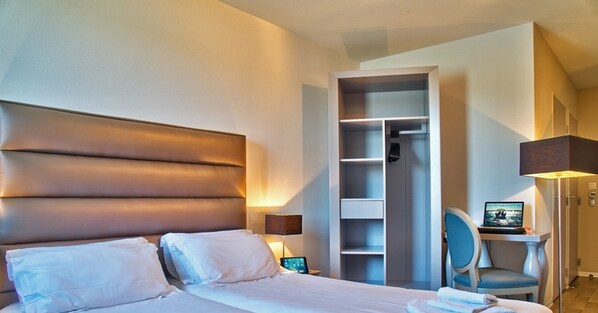Habitació d'hotel amb un llit gran, un armari, una taula de treball amb un ordinador portàtil i una cadira.
