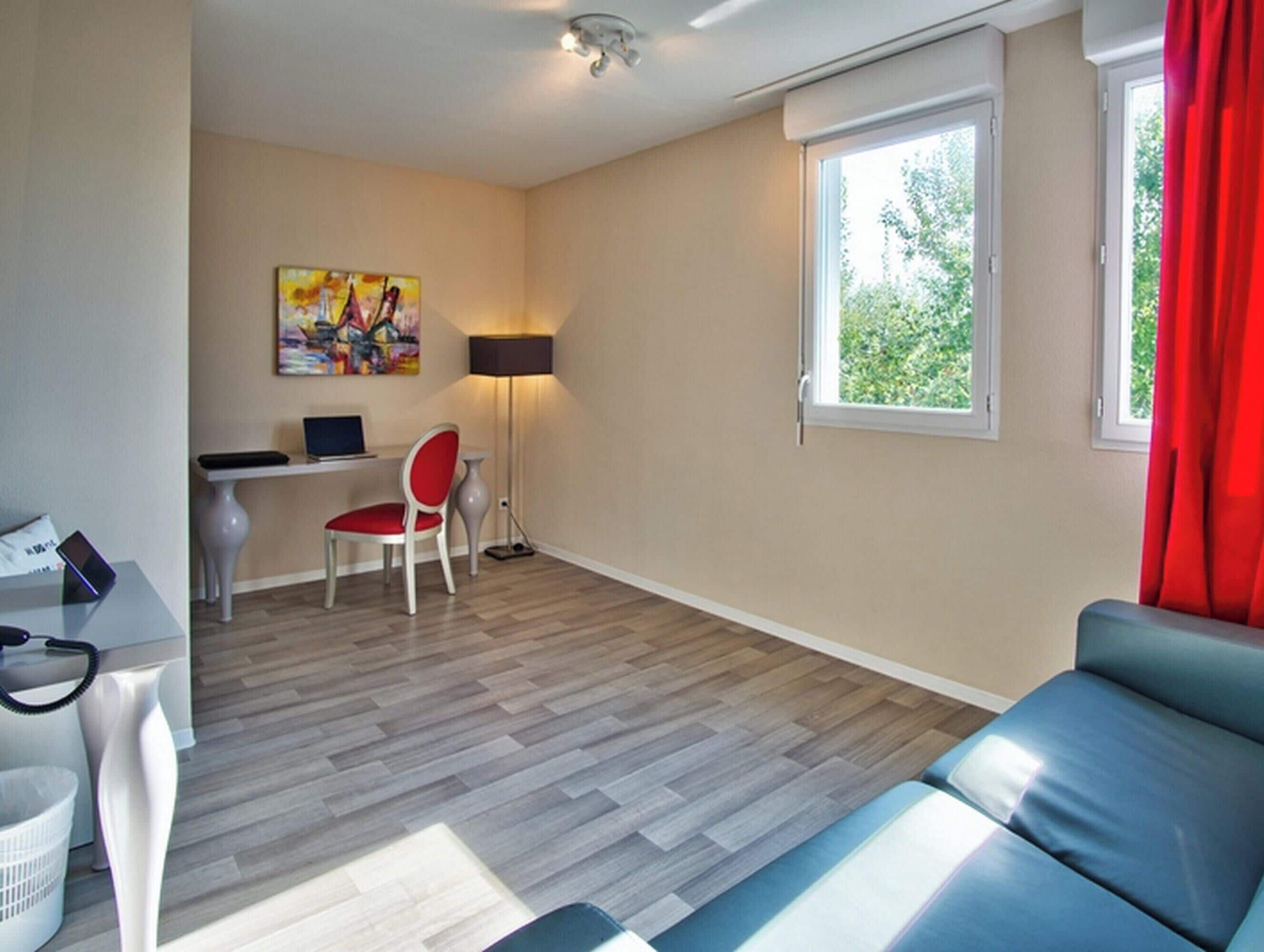 Un salon moderne avec un canapé, un bureau avec un ordinateur, une chaise, une lampe et une fenêtre avec des rideaux.