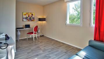 Un salon moderne avec un canapé, un bureau avec un ordinateur, une chaise, une lampe et une fenêtre avec des rideaux.
