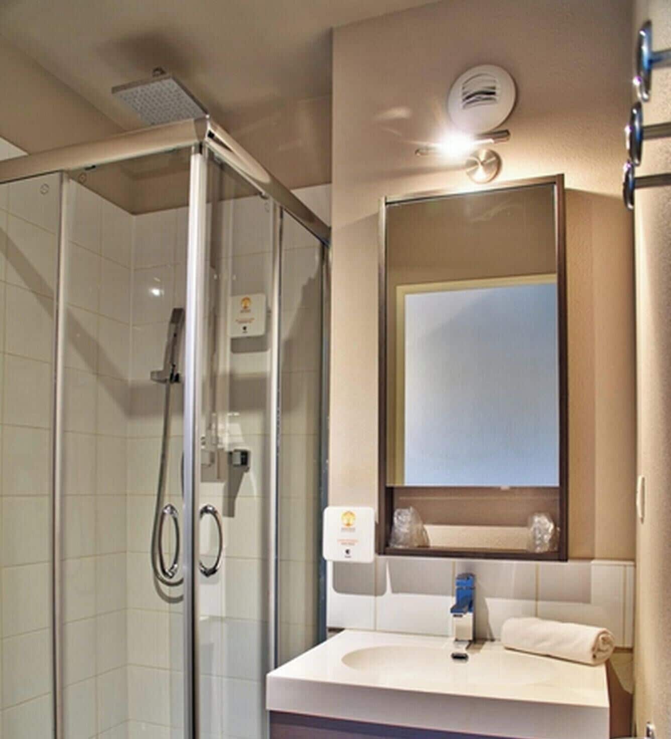 A hotel bathroom with a glass-enclosed shower, a sink with a mirror, and a towel rack.