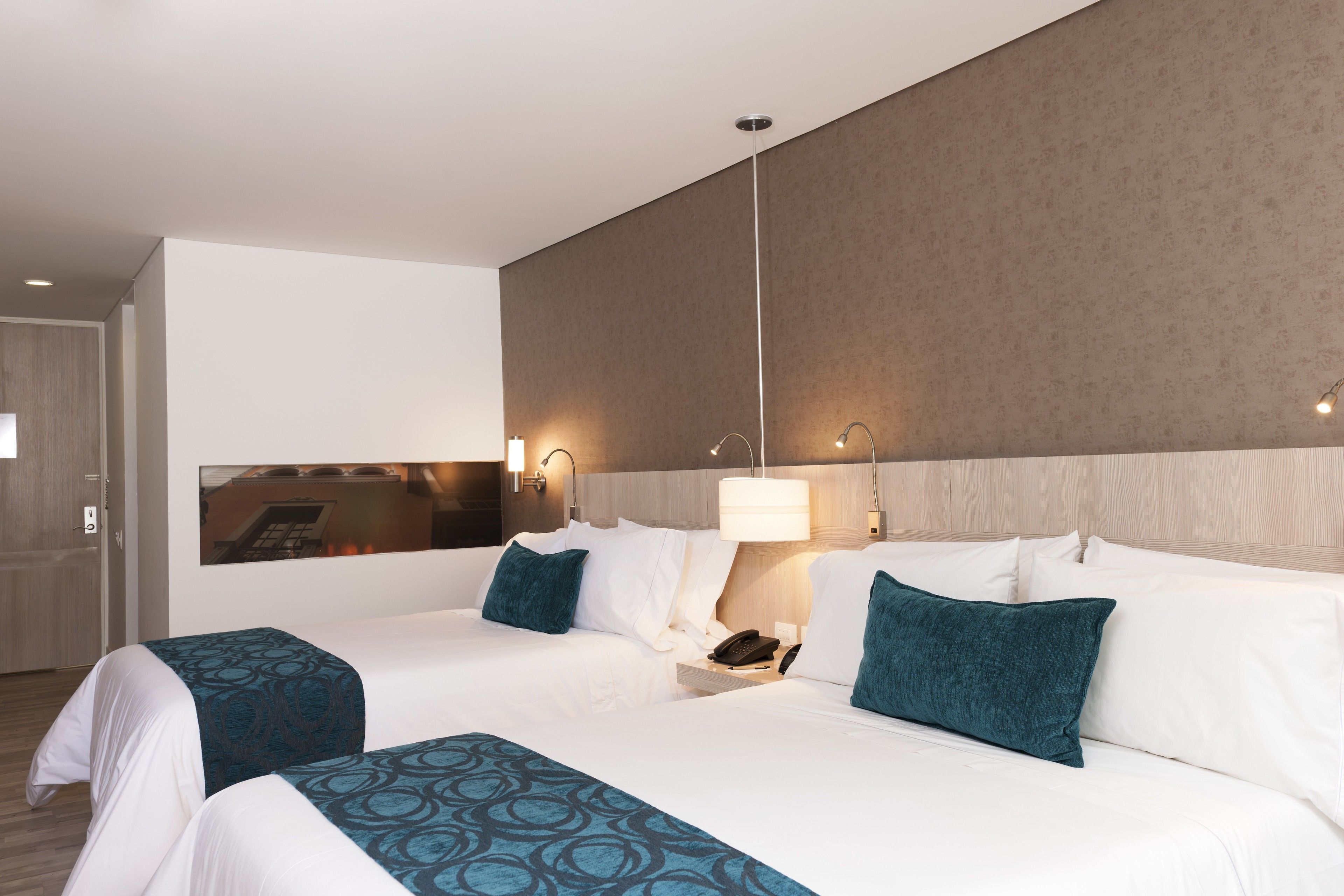 A hotel room with two beds, a nightstand, a lamp, and a wall-mounted phone.