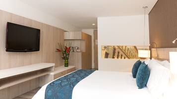 A modern hotel room with a flat-screen TV mounted on the wall, a bed with blue and white bedding, a bedside table, and a small desk area.
