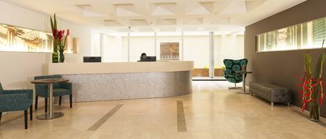 A reception area with a curved counter, teal patterned chairs, a round table, and a grey sofa.