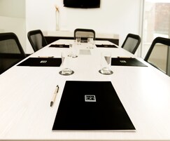 Un salón de conferencias con una larga mesa, individuales negros y vasos transparentes.