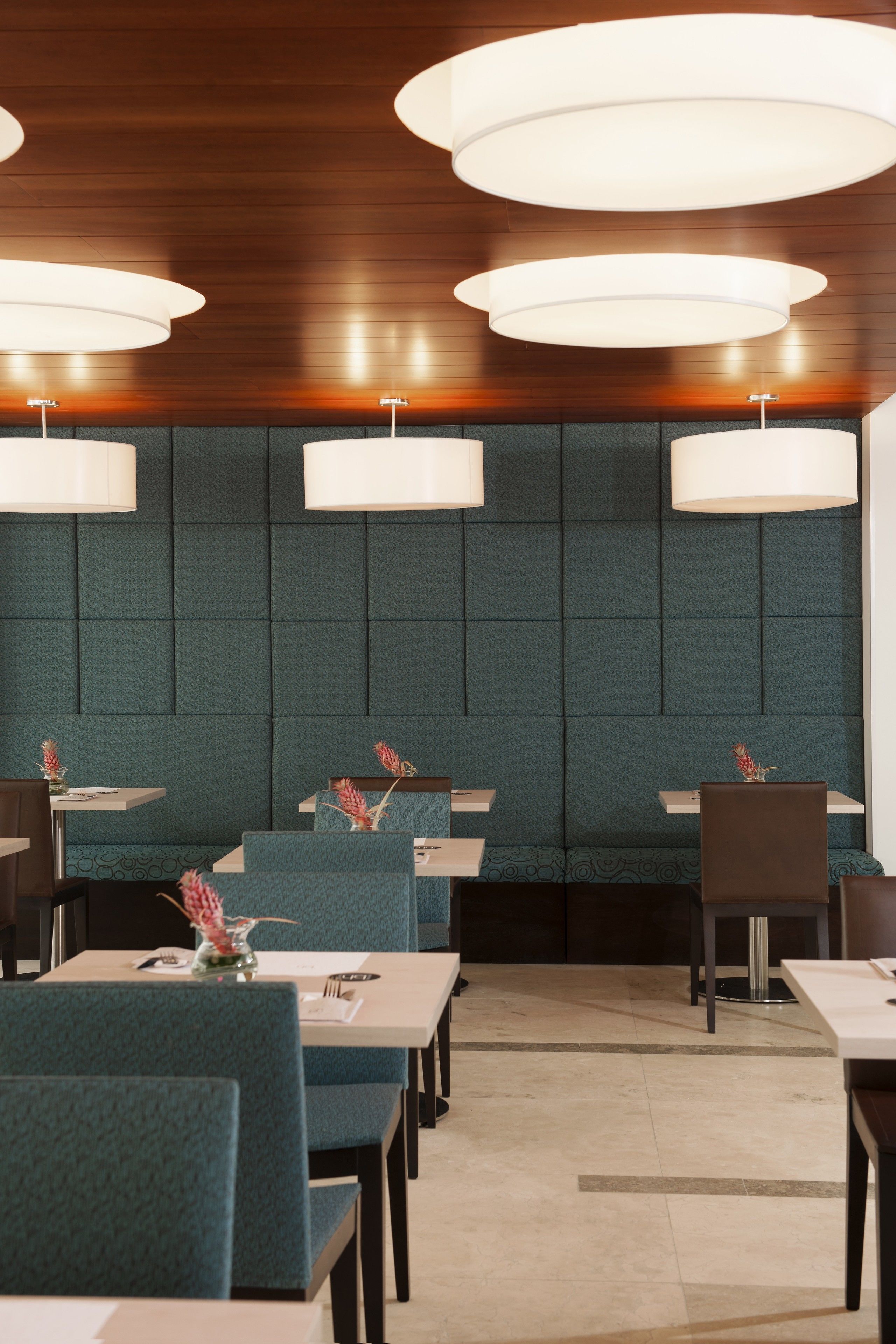A restaurant with booths and tables, wooden ceiling, and pendant lighting.