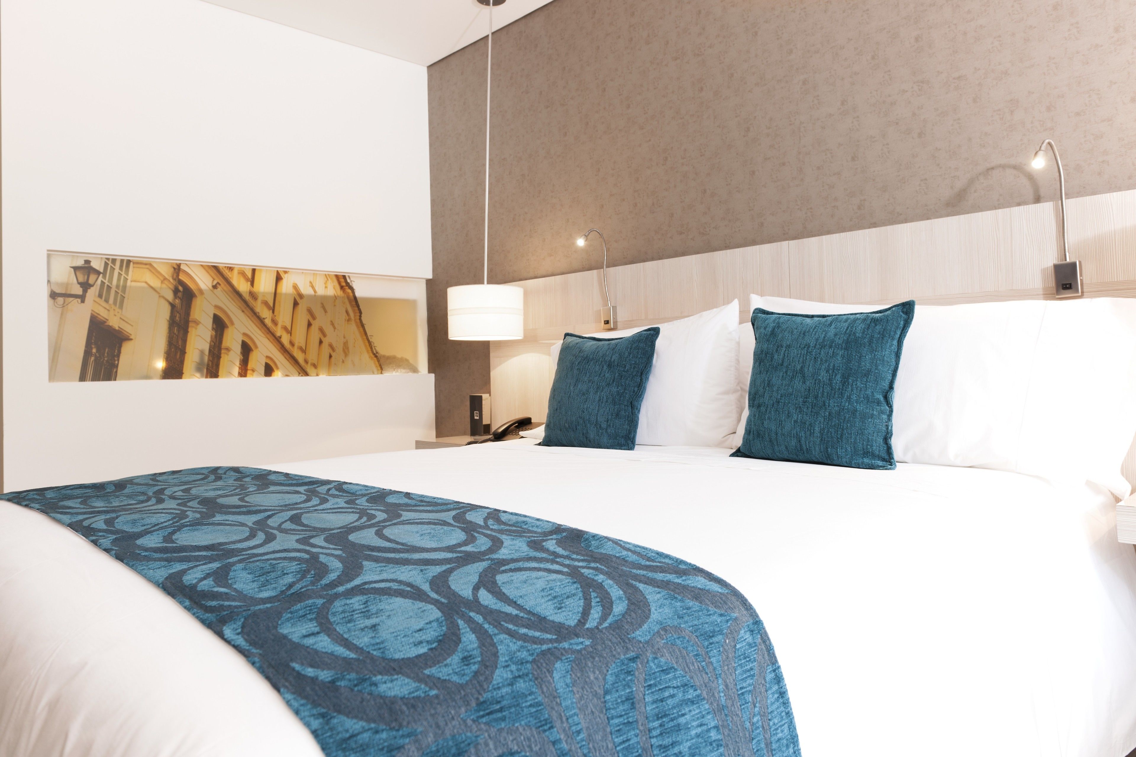 Una habitación de hotel con una cama grande, una mesita de noche con lámpara y un teléfono en la pared.