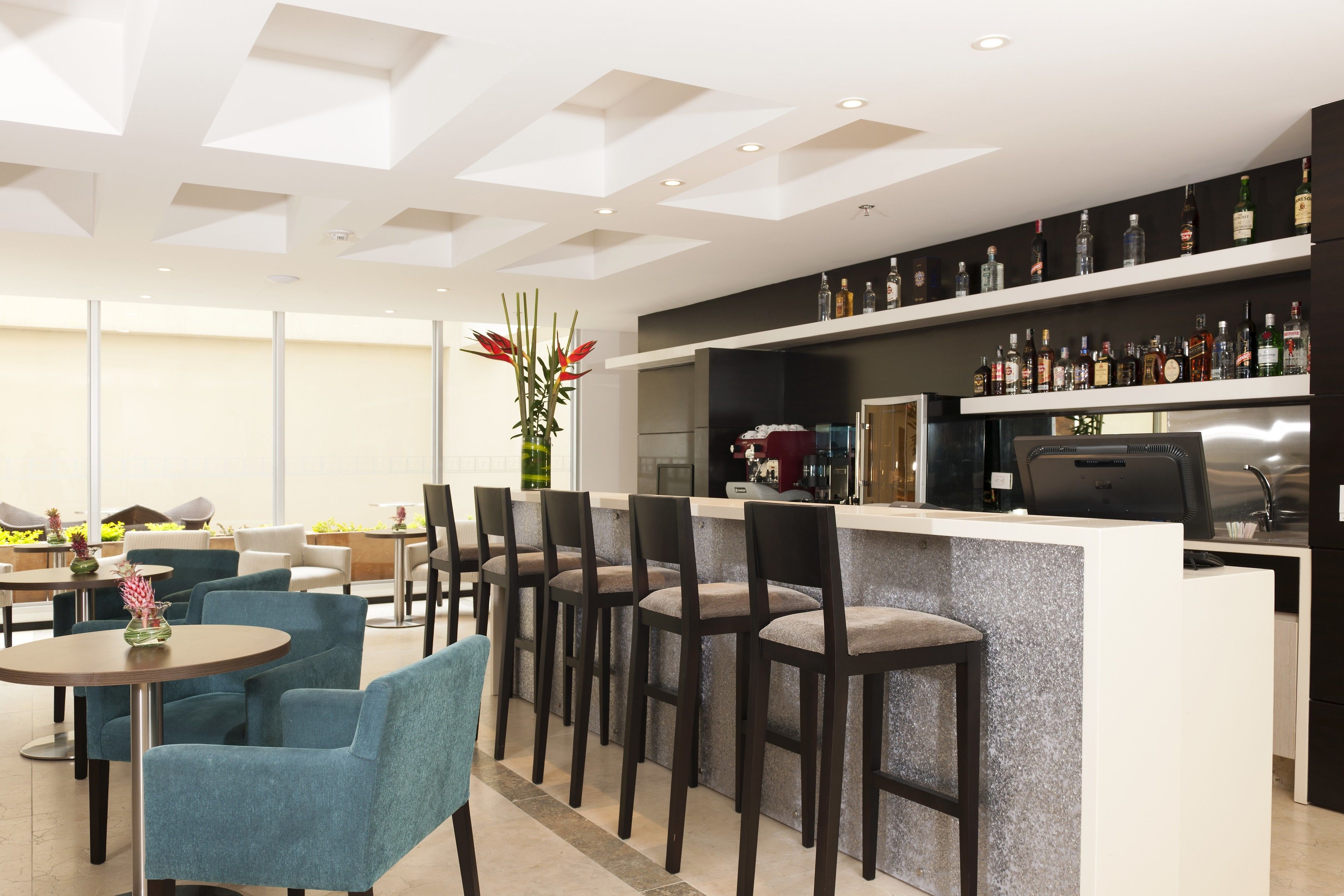 A modern bar area with a counter, bar stools, and a variety of liquor bottles.