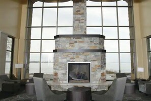Una chimenea de piedra con recinto de vidrio, ventanas amplias y vistas al exterior.