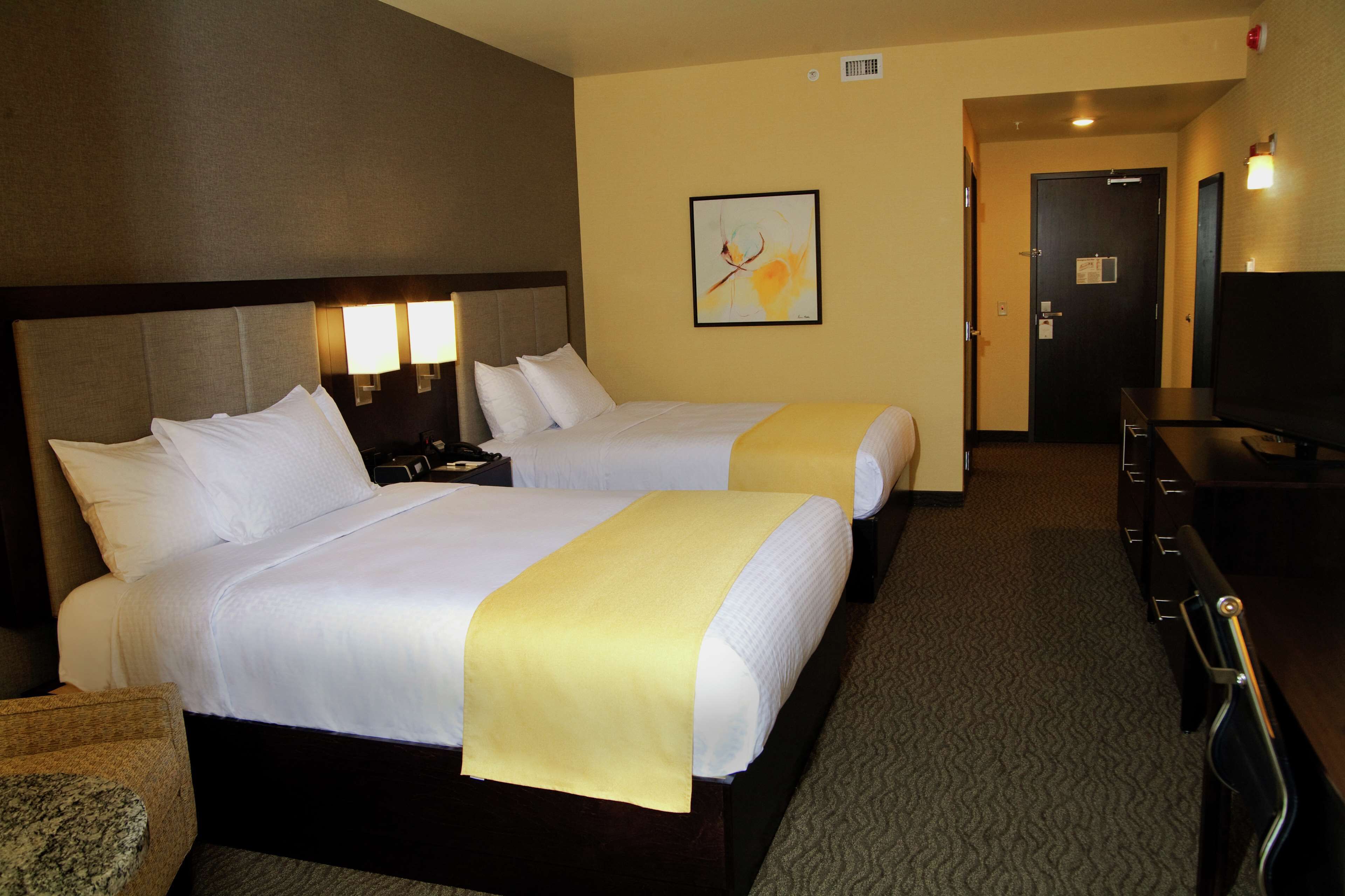 A hotel room with two beds, a desk, a TV, and a door.